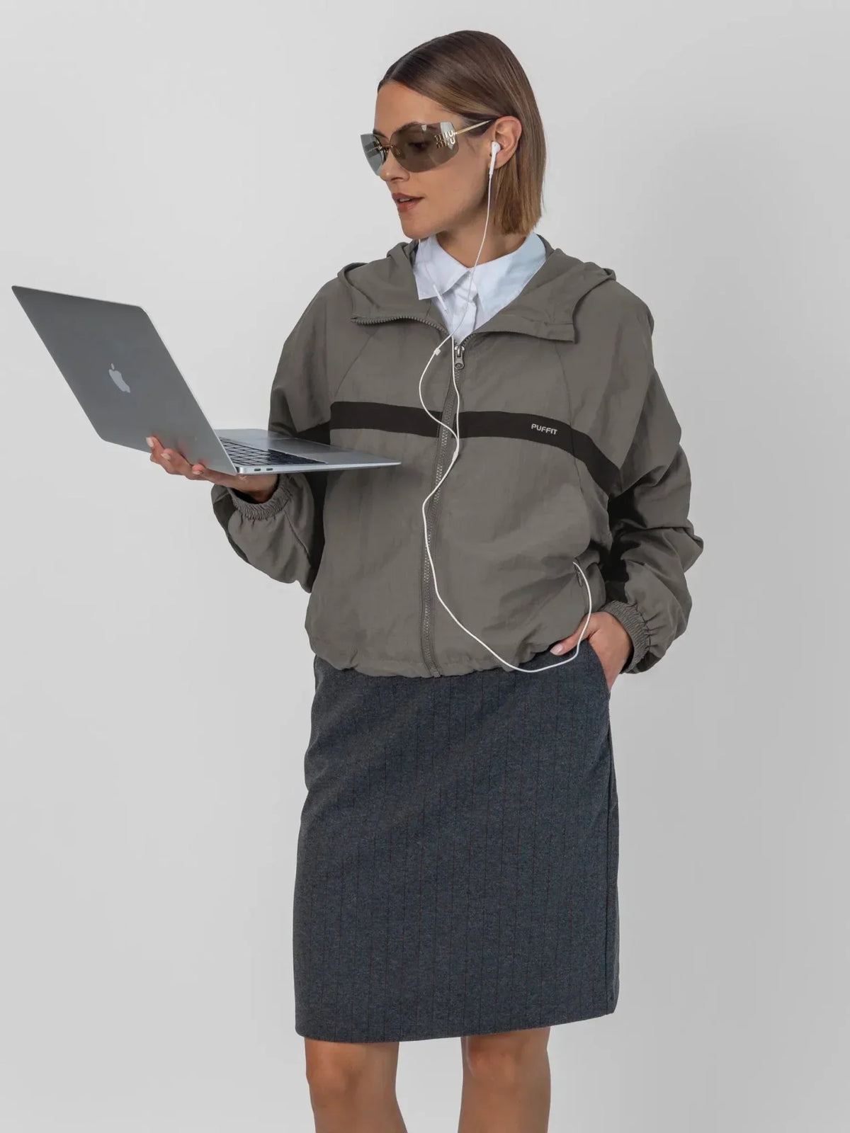 Woman wearing PUFFLT water repellent oversized short track jacket and sunglasses holding a laptop.
