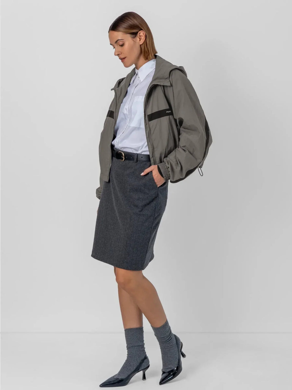 Woman wearing a PUFFLT water repellent oversized short track jacket with a white shirt and grey skirt