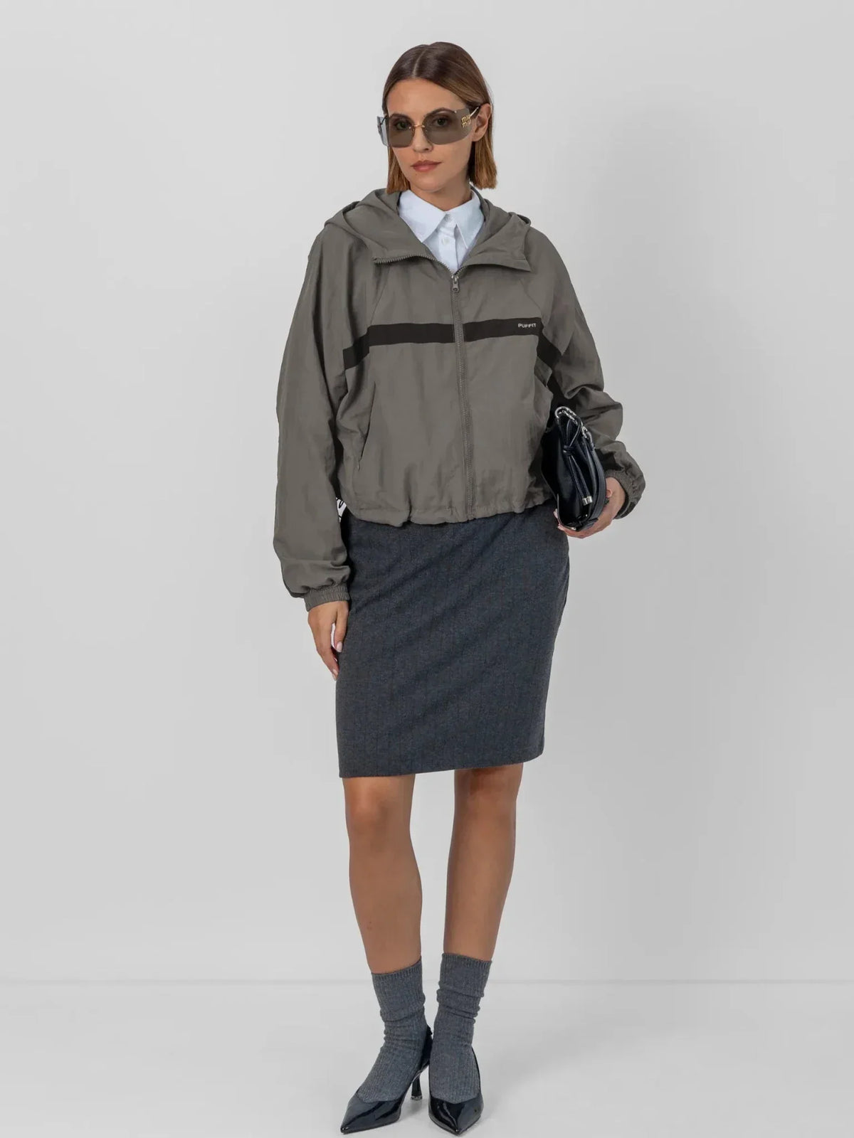 Woman wearing a PUFFLT water repellent oversized short track jacket and grey skirt.