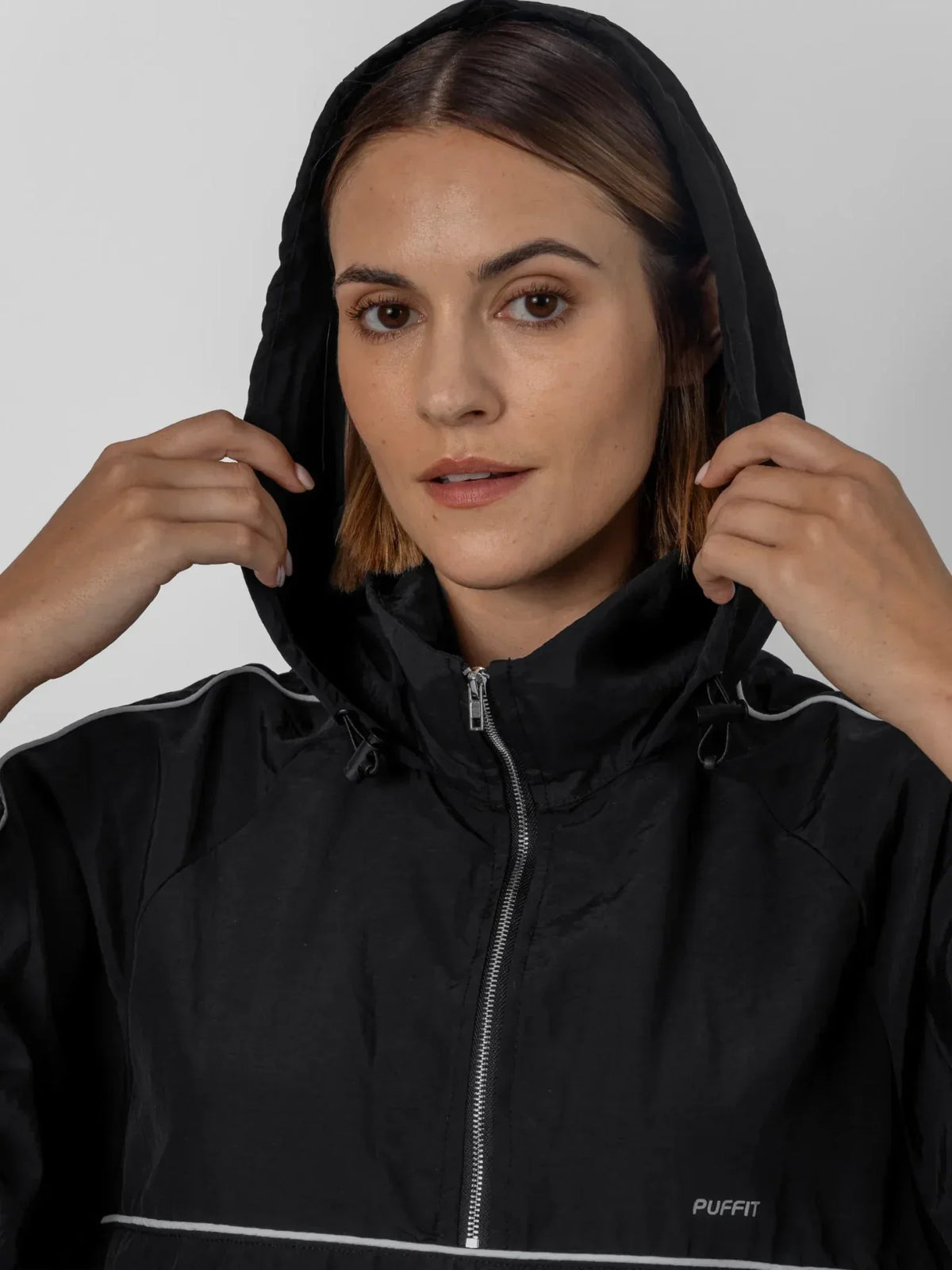 Woman wearing a black PUFFLT water repellent packable-hood track anorak jacket.