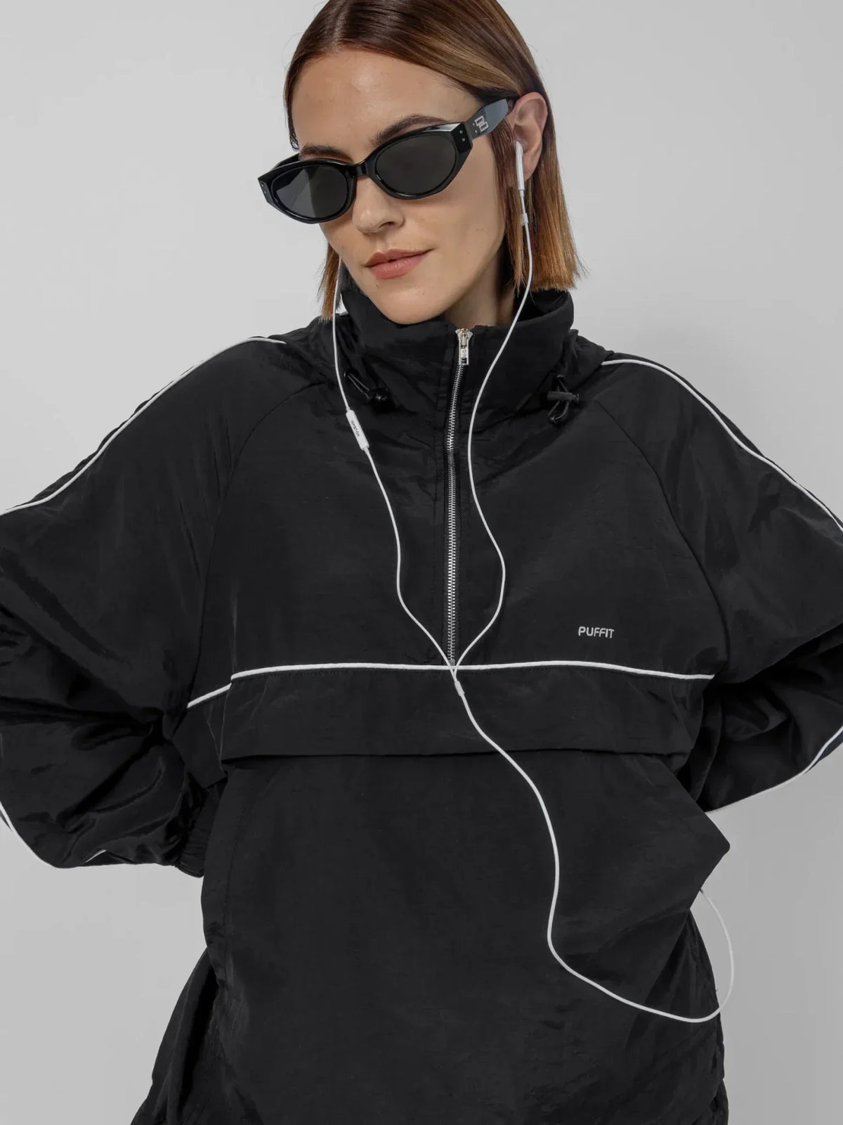 Woman wearing PUFFLT black water repellent packable-hood track anorak and sunglasses.