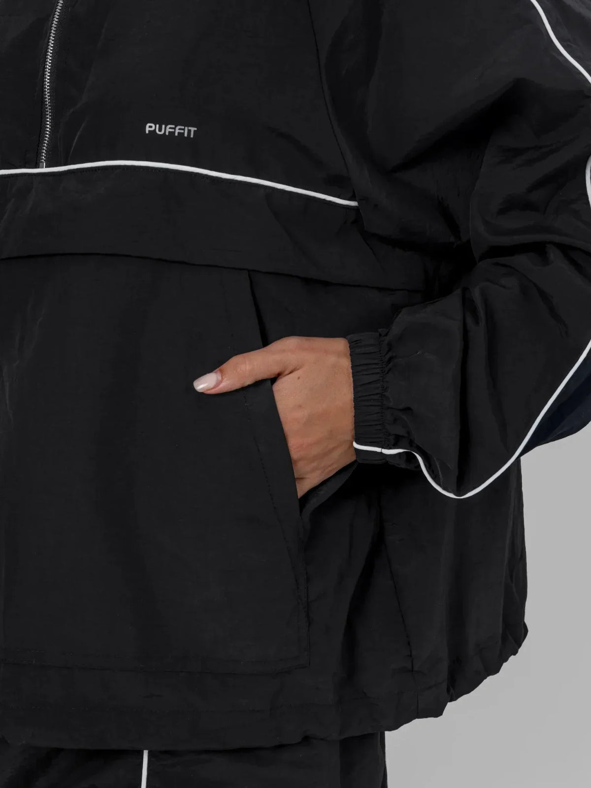 Close up of a person wearing a black PUFFLT water repellent packable-hood track anorak with a hand in the pocket.