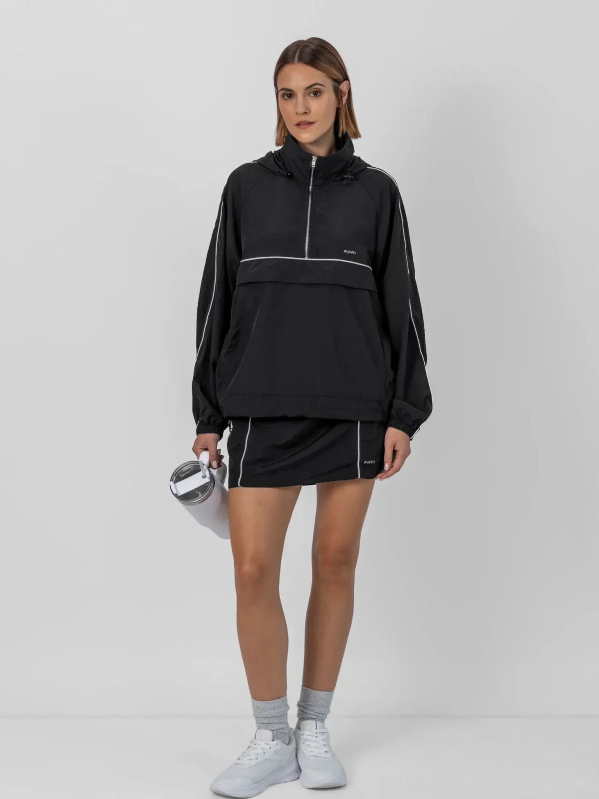 Woman wearing a PUFFLT black water repellent packable-hood track anorak and matching shorts.