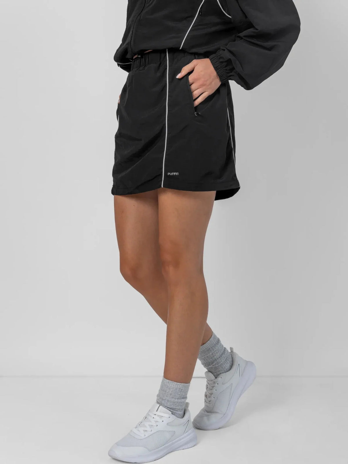 Person wearing PUFFLT black water repellent track shorts and white sneakers.
