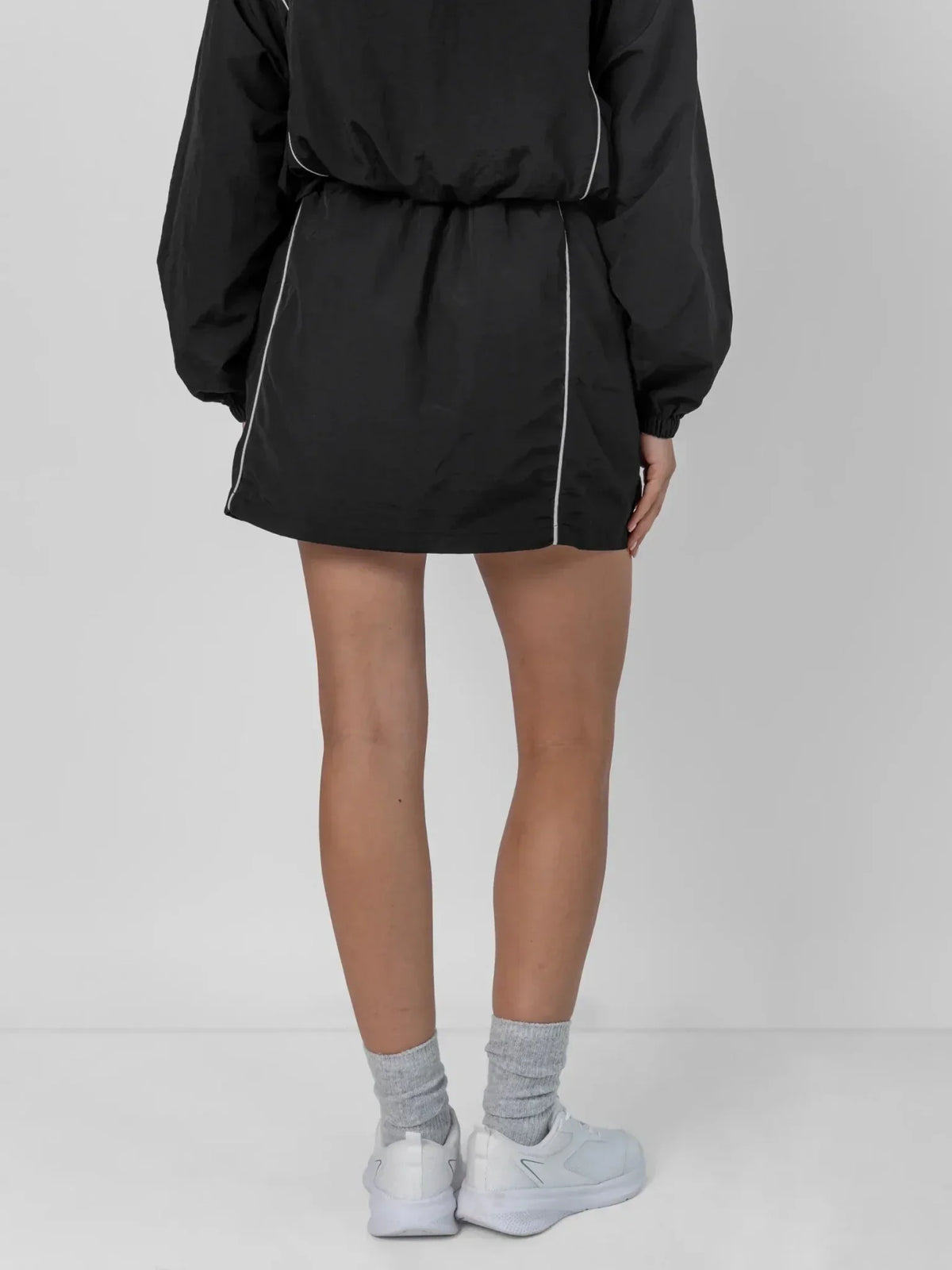 Back view of PUFFLT water repellent regular fit track skirt in black with white piping.