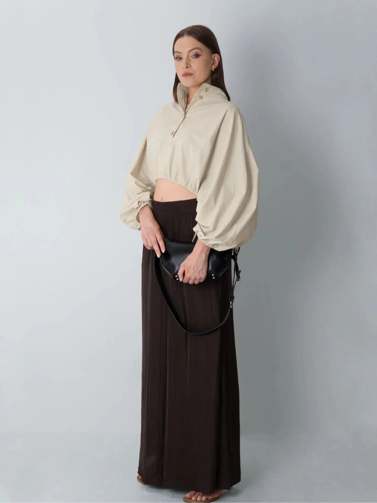 Woman wearing a PUFFLT beige drawstring waist blouse and long brown skirt holding a black bag.