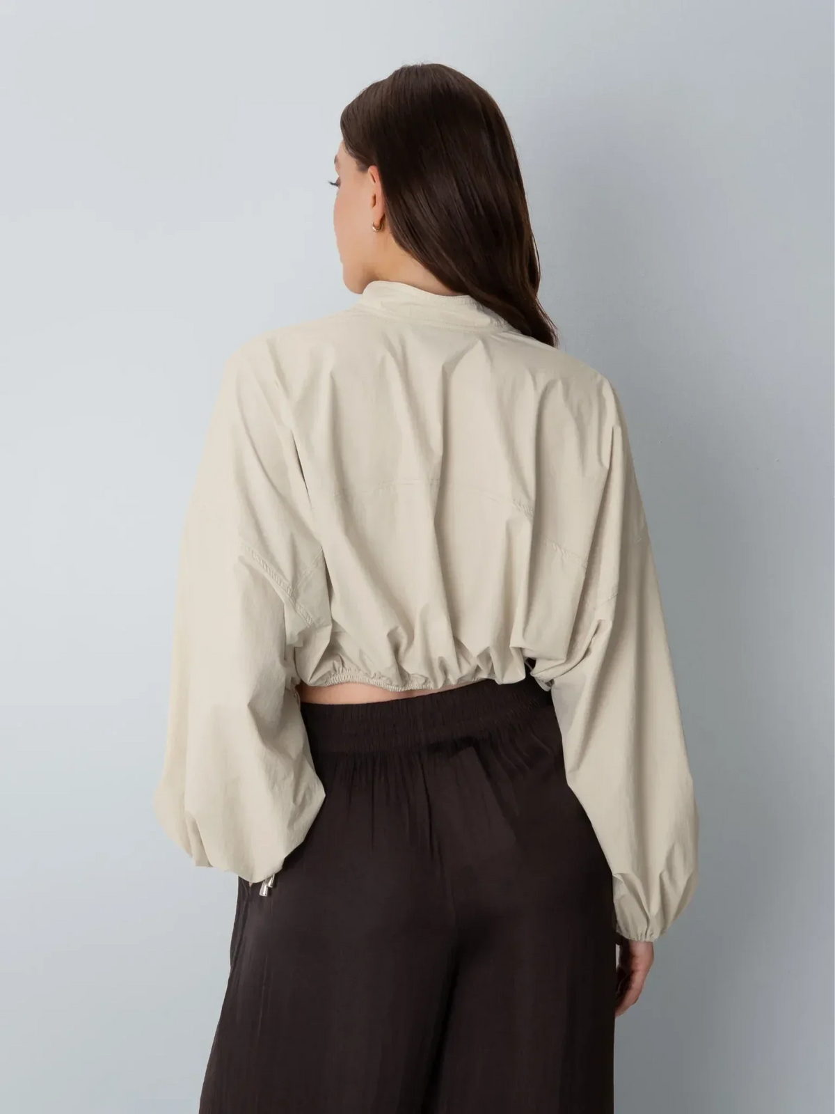 Back view of a PUFFLT drawstring waist cream blouse paired with dark brown trousers.