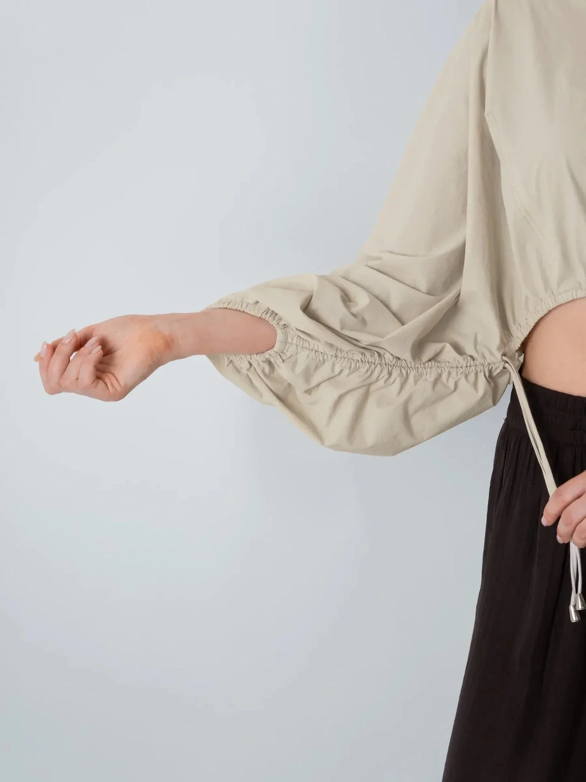 Close-up of the elastic gathered cuff and long sleeve of a beige PUFFLT drawstring waist blouse.