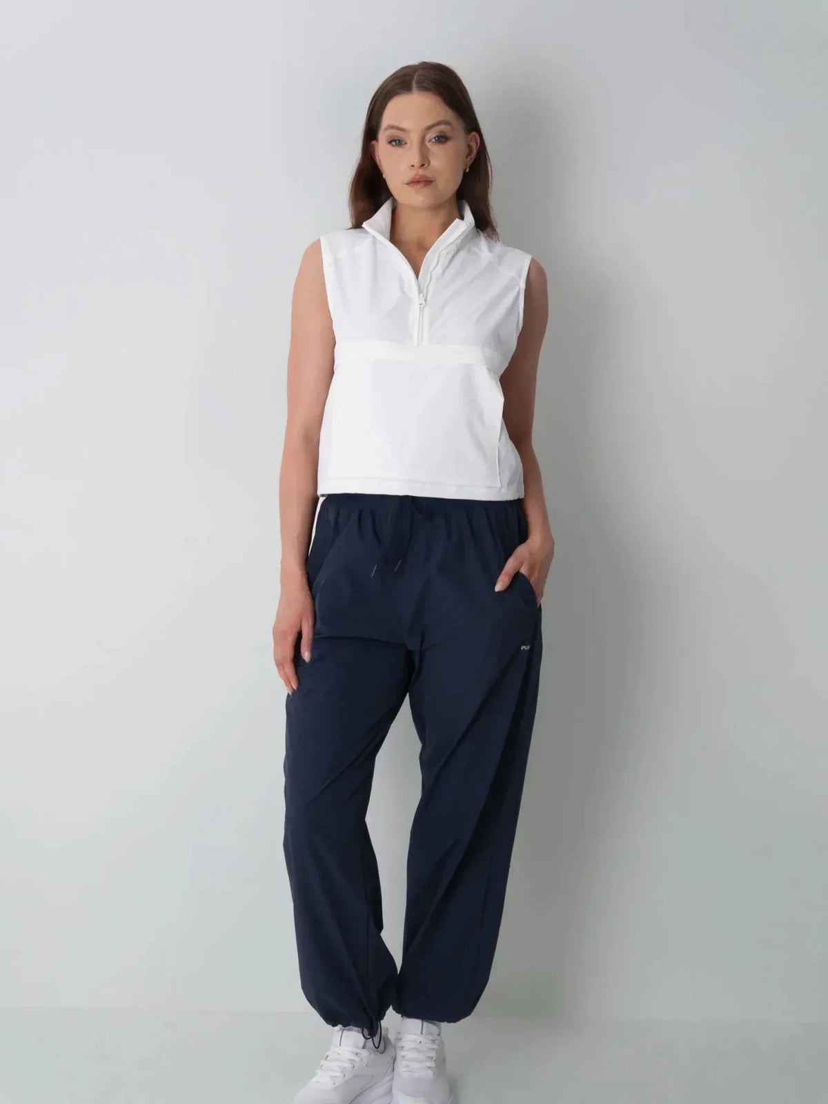 Woman wearing PUFFLT high waisted drawstring utility trousers and a white sleeveless vest.